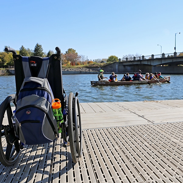 Wheelchair in foreground with canoe full of paddlers in background